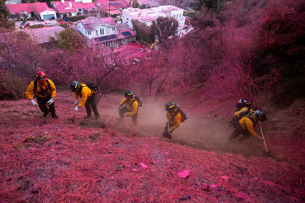 Bombeiros trabalham para limpar um corta-fogo em encosta coberta por retardante rosa de fogo em Mandeville Canyon, bairro de Los Angeles atingido por um dos incêndios simultâneos que devastaram a cidade — Foto: Ringo Chiu/Reuters