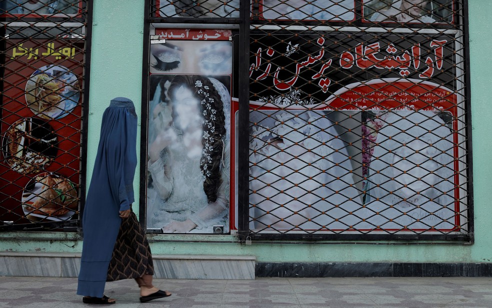 Mulher usando burca passa em frente a vitrine com imagens de modelos pintadas de branco, em Cabul, no Afeganisto, em 6 de outubro  — Foto: Reuters/Jorge Silva