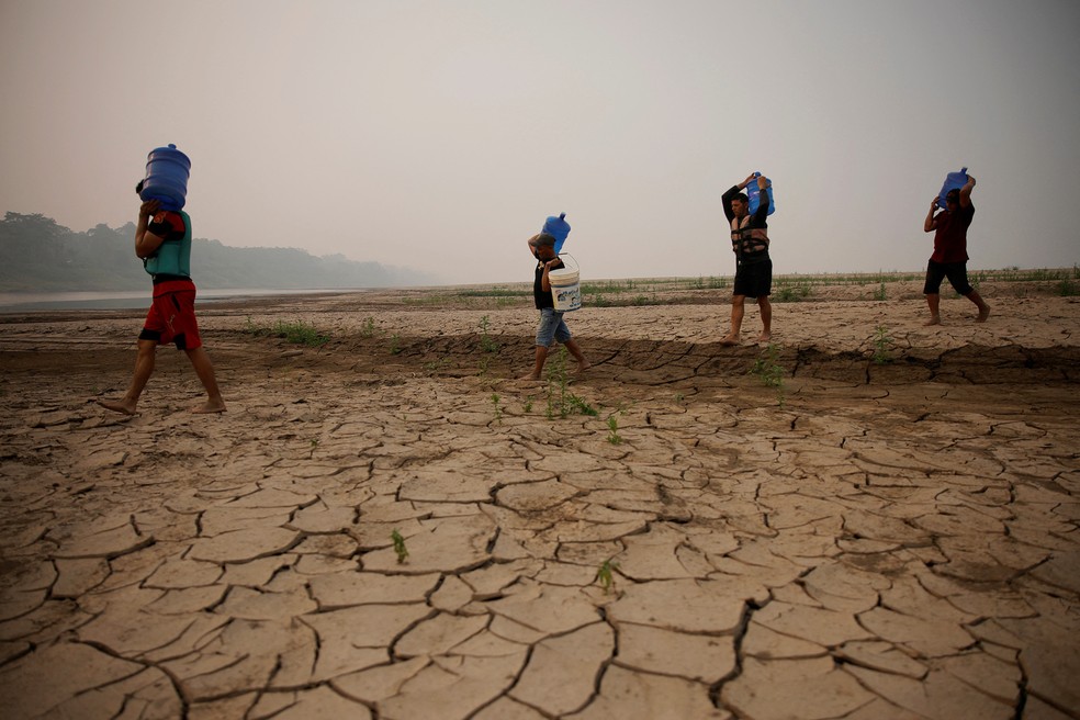 Ribeirinhos carregam galões de água enquanto atravessam bancos de areia do rio Madeira até a comunidade Paraizinho, em meio à pior seca da história. Humaitá, Amazonas (10 de setembro) — Foto: Bruno Kelly/Reuters