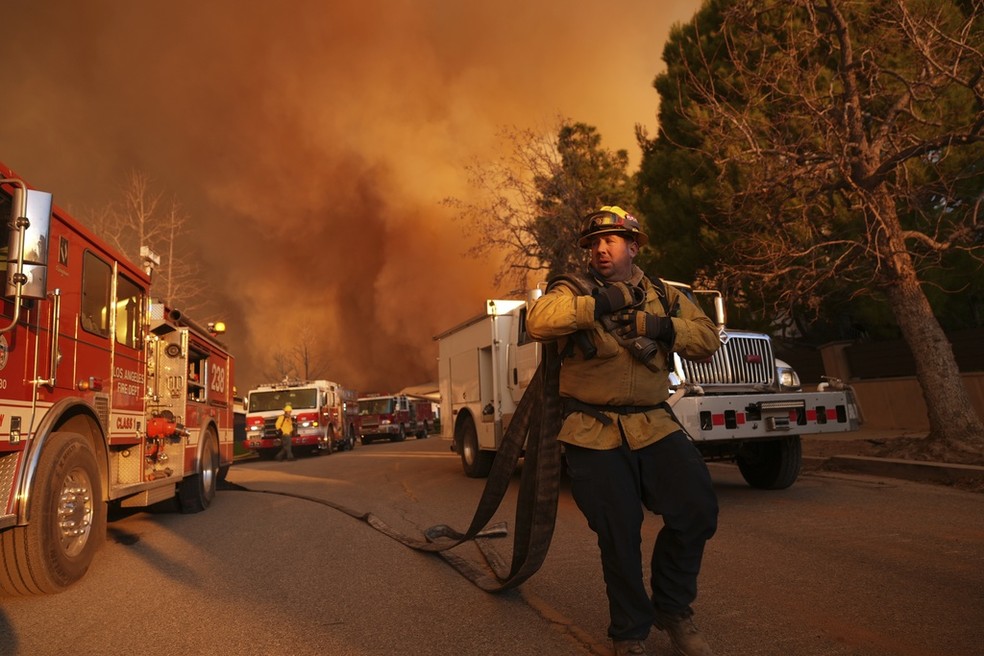 Bombeiro carrega mangueiras diante de incêndio em Palisades, em Los Angeles, nos EUA, em 11 de janeiro de 2025. — Foto: Jae C. Hong/ AP