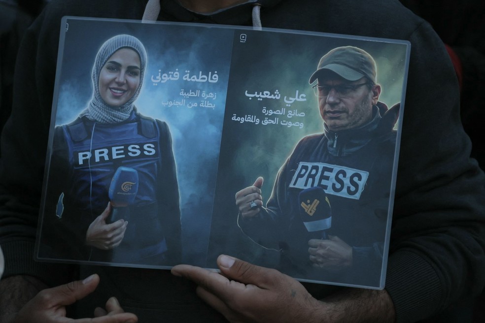 Jornalista segura fotos de Fatima Ftouni e Ali Shaib, mortos por Israel em ataque aéreo no sul do Líbano em 28 de março de 2026 — Foto: IBRAHIM AMRO / AFP