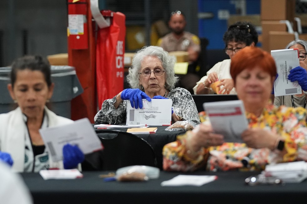 Funcionários eleitorais separam cédulas de voto por correio no escritório do Supervisor de Eleições do Condado de Miami-Dade para as eleições primárias da Flórida, em 18 de agosto de 2026 — Foto: AP Photo/Lynne Sladky