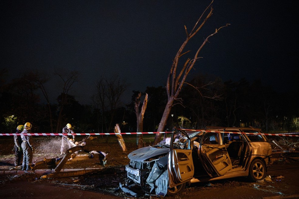 Equipes de resgate ucranianas removem árvores caídas perto de um carro destruído em uma estrada em Kiev. — Foto: Genya Savilov/AFP