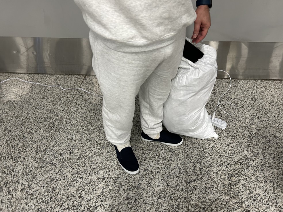 Brasileiro deportado dos EUA carrega celular para falar com a família após desembarcar em Confins — Foto: Rafaela Mansur/ g1