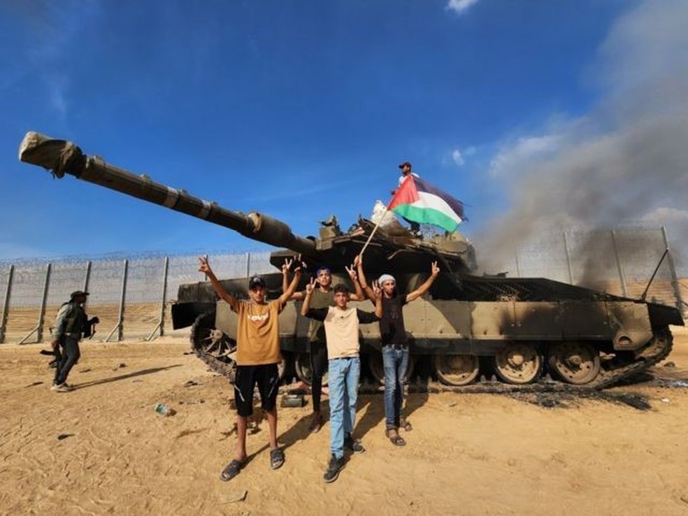 O braço armado do Hamas, as Brigadas Izz ad-Din al-Qassam, seguram uma bandeira palestina enquanto destroem um tanque das forças israelenses em Gaza — Foto: Getty Images/Via BBC