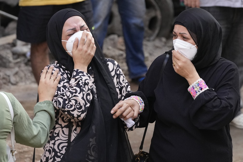 Mulheres choram em frente ao seu apartamento destruído no local do ataque aéreo israelense — Foto: AP/Hassan Ammar