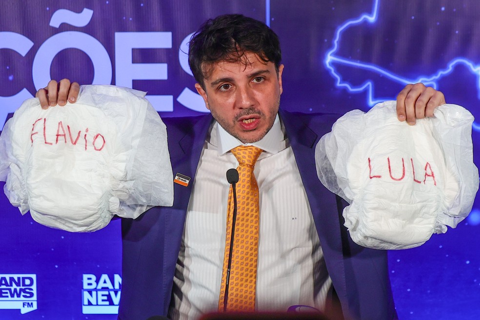 Renan Santos (Missão), segura fraldas com os nomes de Flávio e Lula ao chegar no debate da Band. — Foto: YURI MURAKAMI/ESTADÃO CONTEÚDO