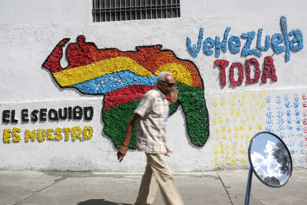 Homem caminha diante de muro com mensagem reivindicado a região guianesa de Essequibo como venezuelana, em Caracas, em 29 de novembro de 2023. — Foto: Matias Delacroix/ AP