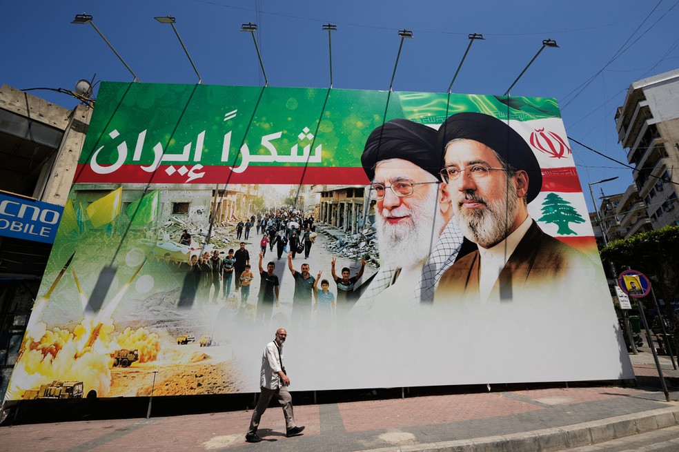 Homem passa por outdoor que mostra fotos do ex-líder iraniano Ali Khamenei e o atual líder supremo, aiatolá Mojtaba Khamenei, com os dizeres em árabe 'Obrigado, Irã', em Dahiyeh, no sul de Beirute, capital do Líbano, no dia 15 de junho de 2026 — Foto: Hussein Malla/AP