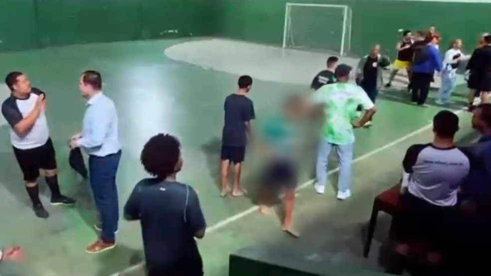 Homem de short amarelo e camisa preta (acima à direita na imagem) foi filmado armado em jogo de futsal — Foto: Reprodução