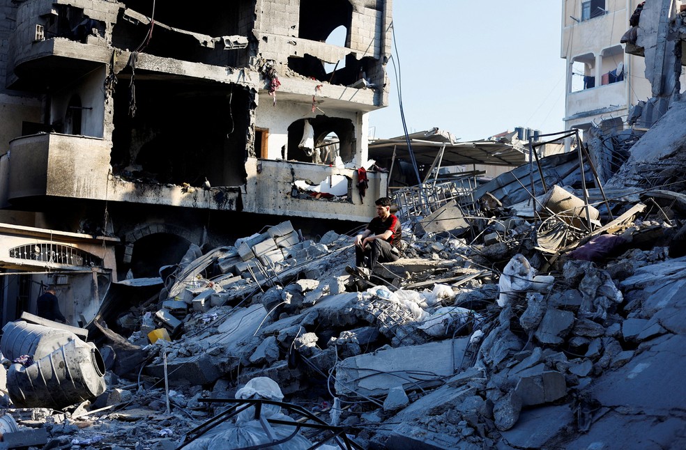 Palestino sentado no topo de escombros de uma casa atingida por um ataque israelense em Deir al-Balah, no centro de Gaza. — Foto: Mahmoud Issa / Reuters
