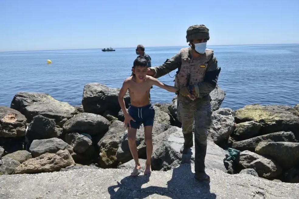  Não é a primeira vez que dezenas de pessoas procedentes do Marrocos tentam chegar a Ceuta a nado. Nesta imagem de 2021, um soldado espanhol auxilia uma criança estrangeira que acaba de chegar a Ceuta nadando — Foto: Antonio Sempere / Getty