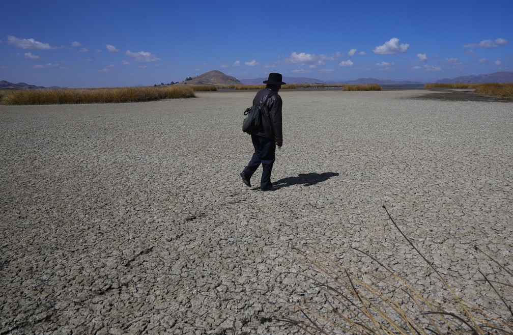 Homem caminha em região seca que pertencia ao lago Titicaca, na Bolívia, em 27 de julho de 2023 — Foto: Juan Karita/AP