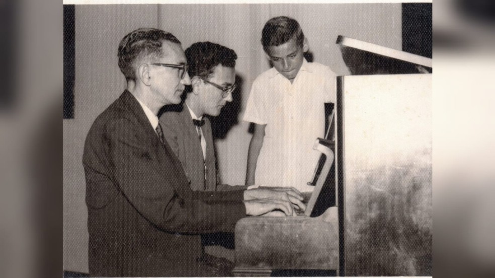 Piano a 4 mãos: Wilson Fonseca e seu filho Vicente Malheiros da Fonseca, sendo observados por José Agostinho da Fonseca (Maestro Tinho), ainda criança - Santarém-PA, 1966 — Foto: Arquivo de família