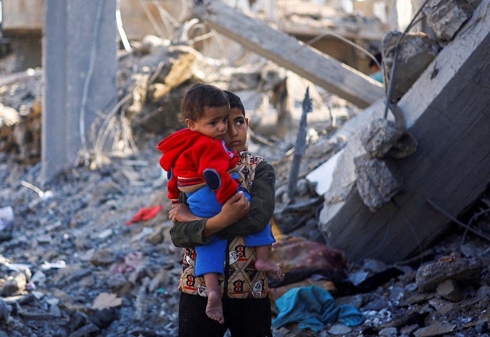 Menino palestino carrega bebê em área bombardeada por Israel na Faixa de Gaza 04/12/2023 — Foto: REUTERS/Mohammed Salem