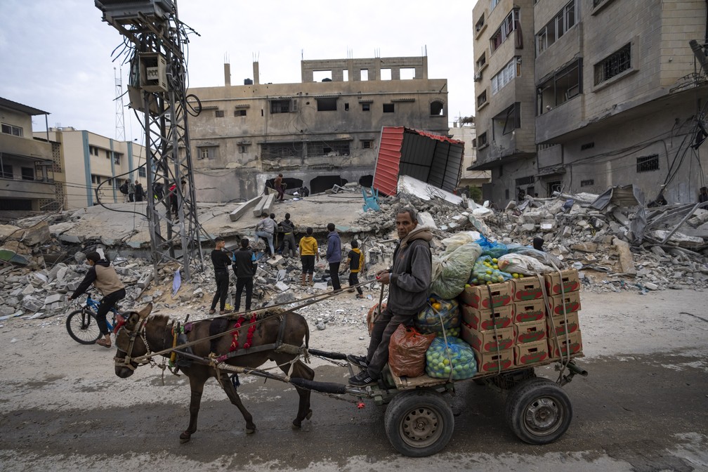 Palestinos são vistos diante de construção atingida por ataque aéreo em Rafah no dia 21 de dezembro de 2023 — Foto: Fatima Shbair/Associated Press
