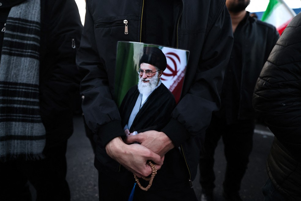 Homem segura cartaz com imagem do aiatolá Ali Khamenei após morte do líder em ataques de EUA e Israel — Foto: Atta Kenare/AFP