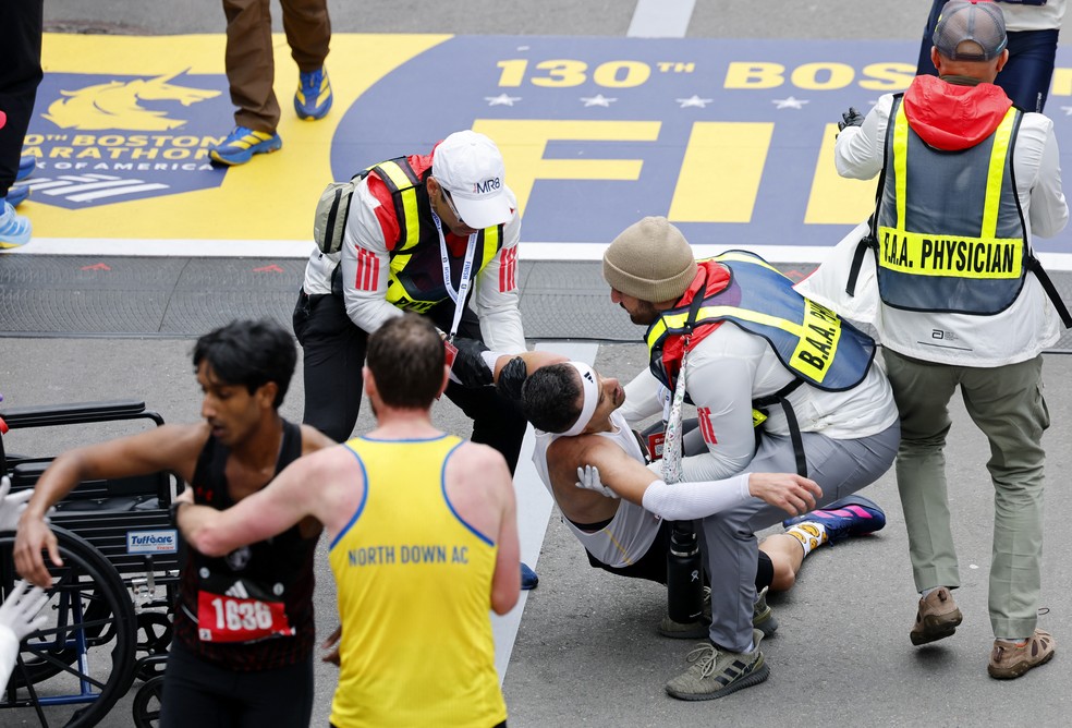 Robson de Oliveira recebe atendimento médico após cruzar a linha de chegada carregando outro corredor na Maratona de Boston — Foto: Reuters/Cj Gunther
