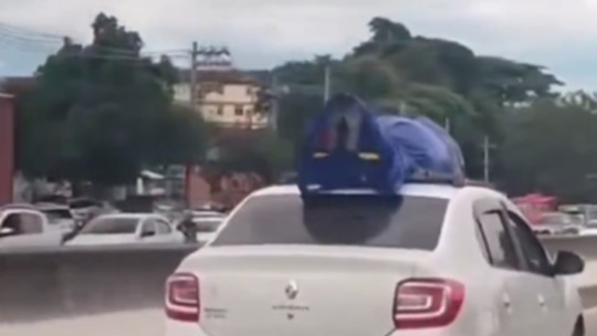 É #FAKE que vídeo mostre transporte de cadáver em teto de carro no Rio - 'No Rio, família opta por transportar cadáver através de um Uber após achar muito caro o frete oferecido pela funerária', diz legenda que tira a gravação de contexto. PM do Rio e bombeiro que estava no veículo confirmaram que se tratava de um manequim, e não de um corpo.