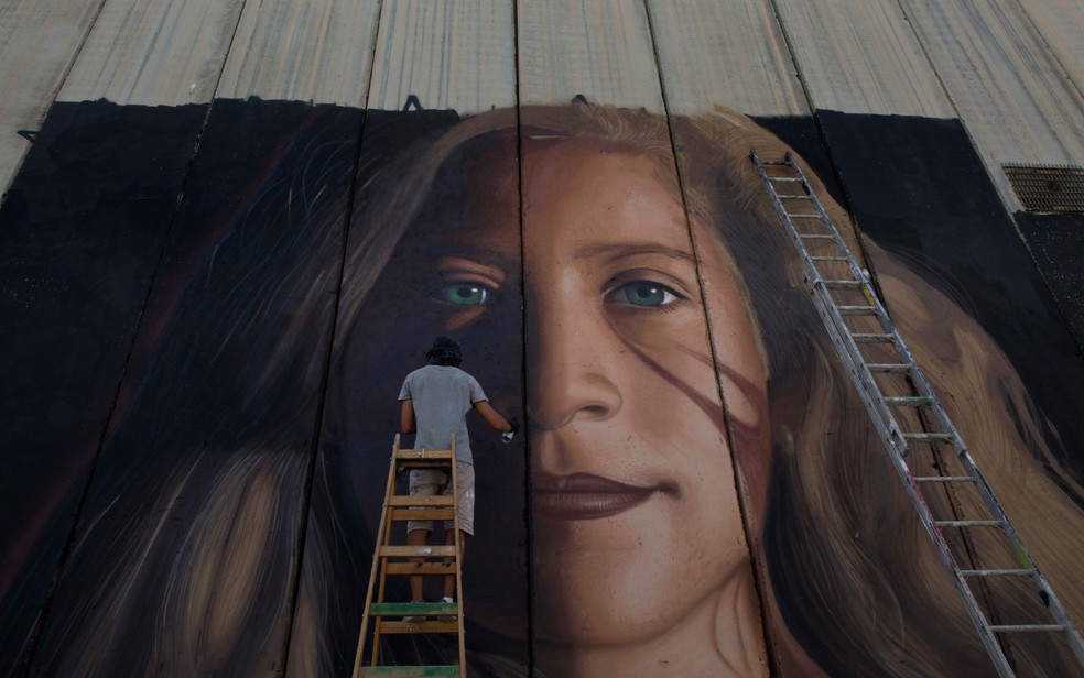 Artista pinta mural com o rosto de Ahed Tamimi no muro de separação de Israel em Bethlehem, na Cisjordânia, no dia 25 de julho — Foto: AP Photo/Nasser Nasser