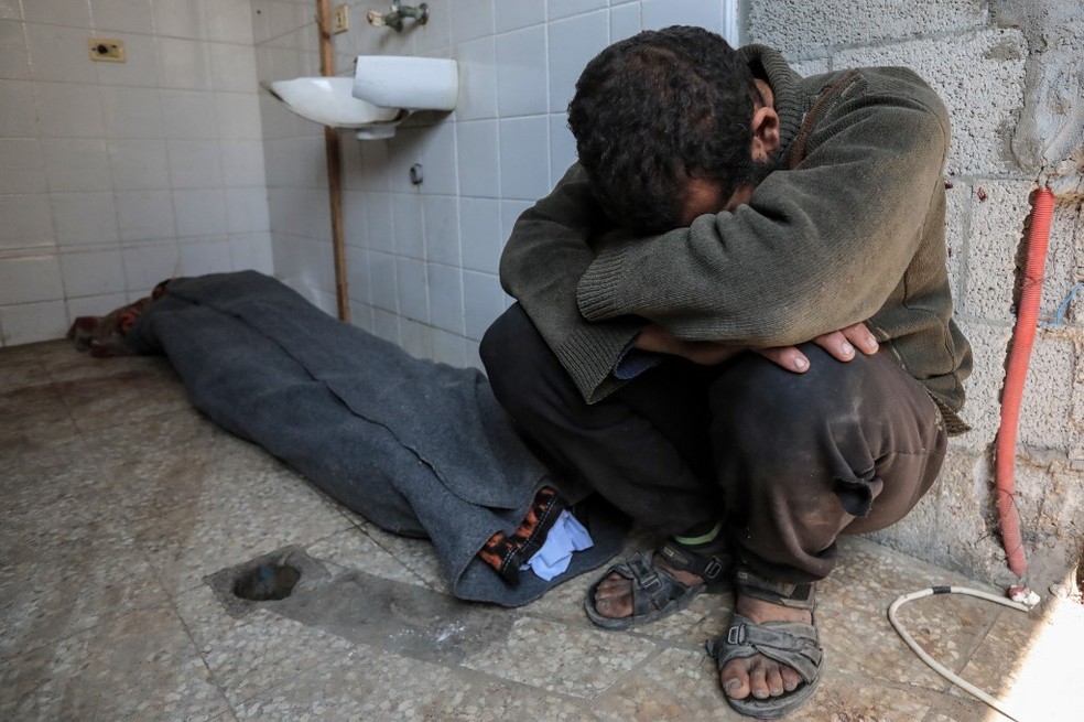 Palestino chora ao lado de corpo de pessoa morta após ataques israelenses em Gaza, no hospital Deir el-Balah — Foto: AFP