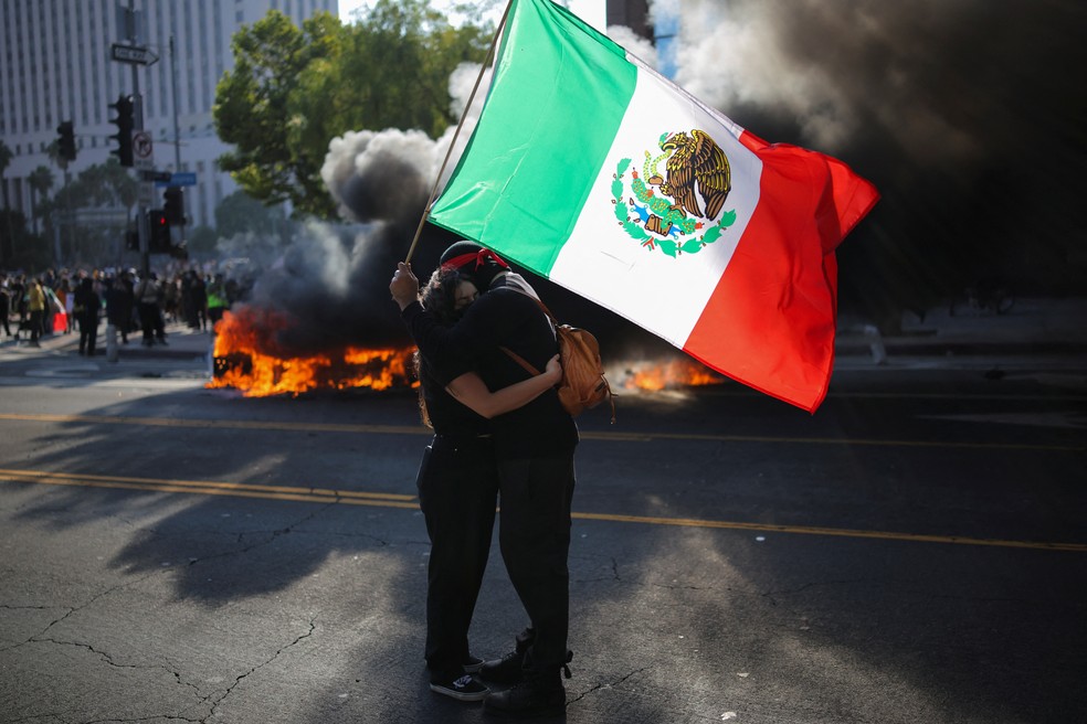 Manifestantes se abraçam sob bandeira do México em protesto na cidade de Los Angeles — Foto: REUTERS/Daniel Cole