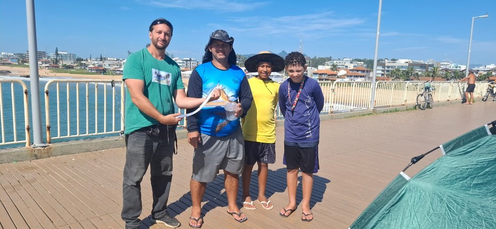 O biólogo Jhones Poubel segurando um peixe-espada ao lado do pescador Pedro (que pescou o peixe que aparece na foto), da esposa de Pedro, Marcele; e do filho de Pedro, Pietro — Foto: Jhones Poubel/Arquivo pessoal