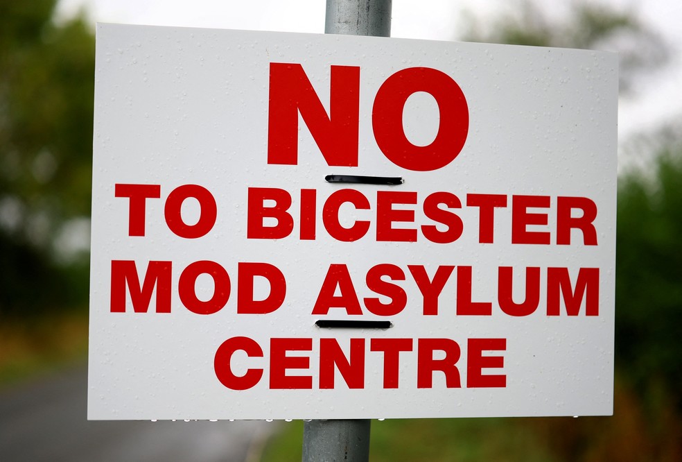 Uma placa contra os planos para um centro de acolhimento de requerentes de asilo em uma antiga base militar próxima é exibida em Piddington, Inglaterra, em 8 de setembro de 2026 — Foto: REUTERS/Hannah McKay