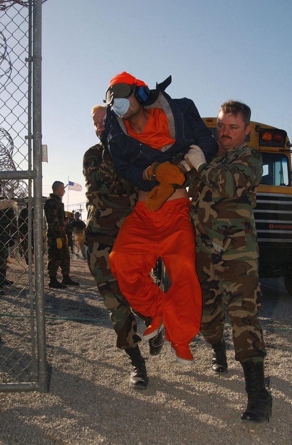 Membros do 115º Batalhão da Polícia Militar carregam um prisioneiro. Os detidos, algemados nos pés e nas mãos e privados de suas capacidades sensoriais, moviam-se com dificuldade e estavam em sua maioria muito magros. Assim, alguns soldados optavam por carregá-los. — Foto: MICHAEL W. PENDERGRASS/USN via BBC