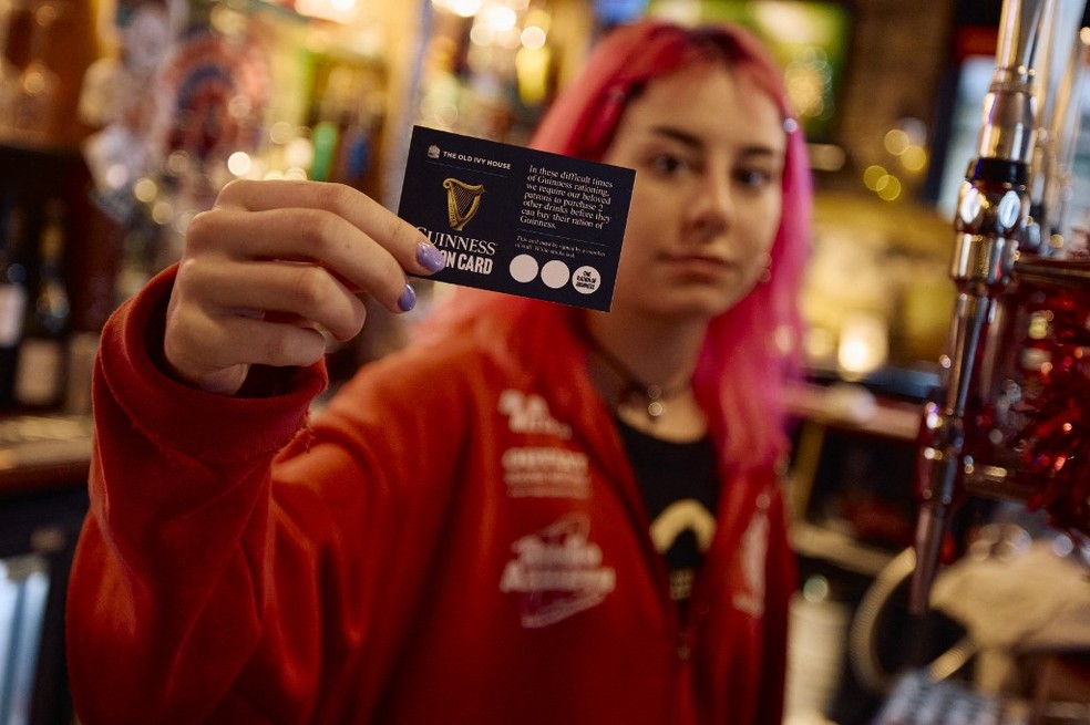 Funcionária de pub em Londres, no Reino Unido, mostra cartão de racionamento de cerveja Guinness. — Foto: Benjamin Cremel/AFP