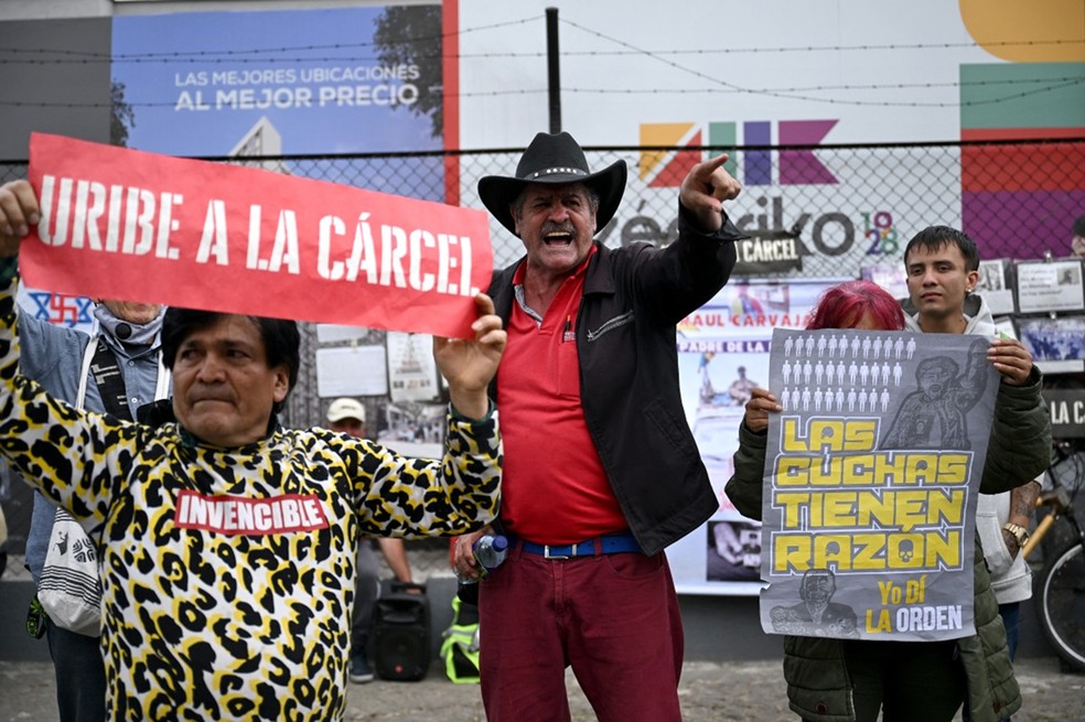 Um homem grita entre pessoas que seguram cartazes contra o ex-presidente colombiano Álvaro Uribe em Bogotá, no dia 28 de julho de 2025 — Foto: Rafael Arboleda/AFP