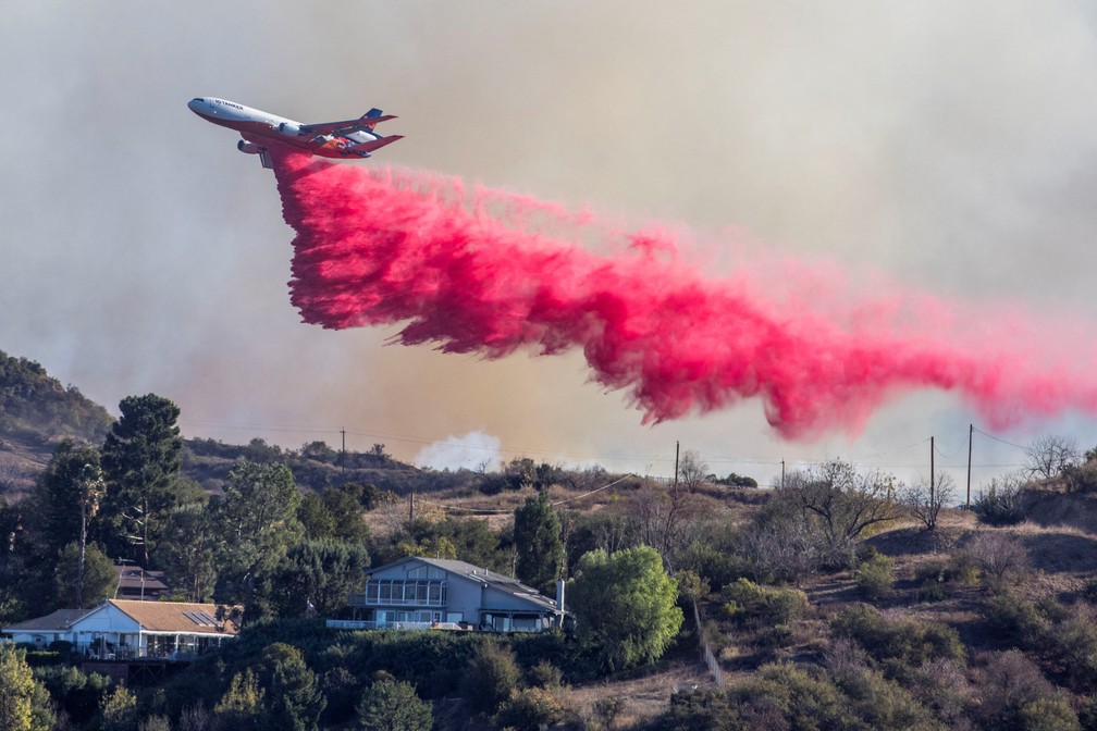 Avião despeja retardante rosa de fogo sobre área atingida por incêndio vista de Woodland Hills, em Los Angeles — Foto: Ringo Chiu/Reuters