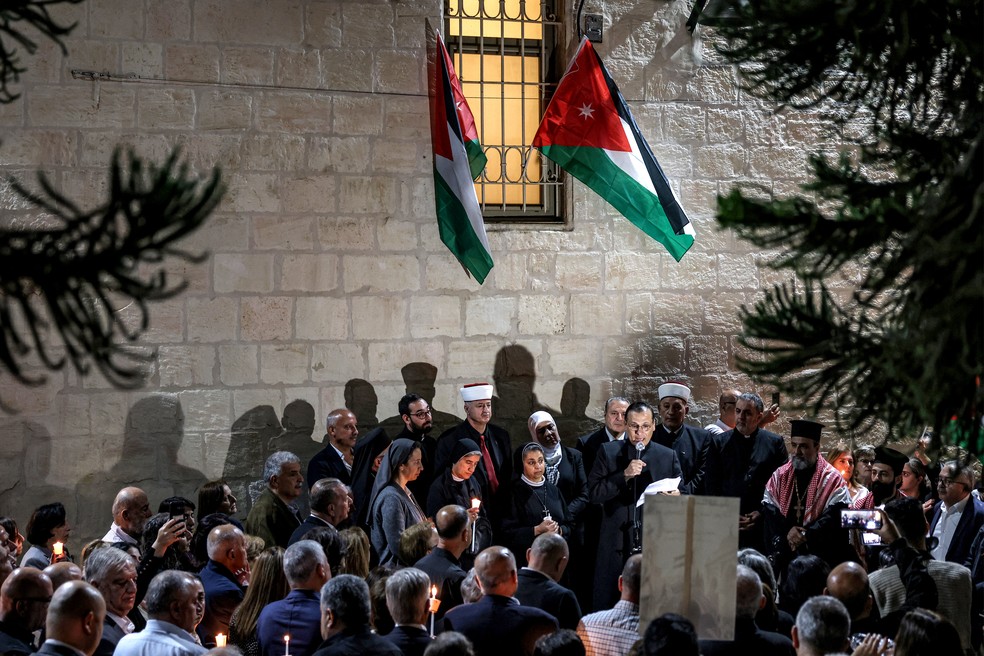 Fiéis ouvem um clérigo cristão discursar durante uma vigília na Igreja Ortodoxa Grega da Transfiguração, na Cisjordânia ocupada por Israel, em 26 de outubro de 2026, em solidariedade às vítimas do ataque à Igreja de São Jorge, em 23 de outubro — Foto: ZAIN JAAFAR / AFP