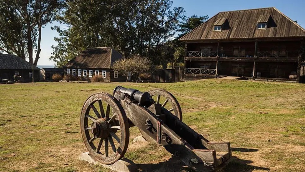 O armazém da Companhia Russo-Americana no Forte Ross (à direita, na imagem), com dois andares, servia também para a venda de produtos. À esquerda, encontram-se residências de colonos. O forte chegou a abrigar no seu auge cerca de 60 construções — Foto: Alamy via BBC