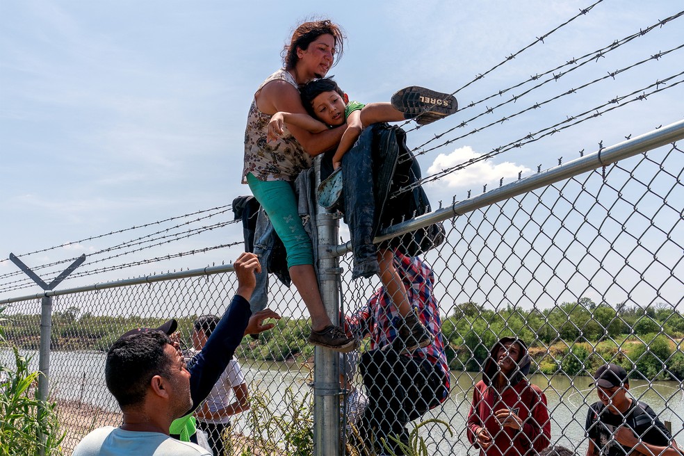 25 de agosto - Migrantes escalam cerca de arame farpado depois de cruzar o Rio Grande vindo do México para os EUA, em Eagle Pass, Texas — Foto: Suzanne Cordeiro/AFP