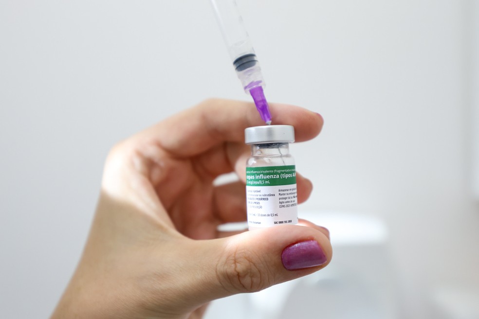 Profissional da saúde segura agulha e frasco de vacinação contra influenza — Foto: Leo Munhoz/Secom/Divulgação