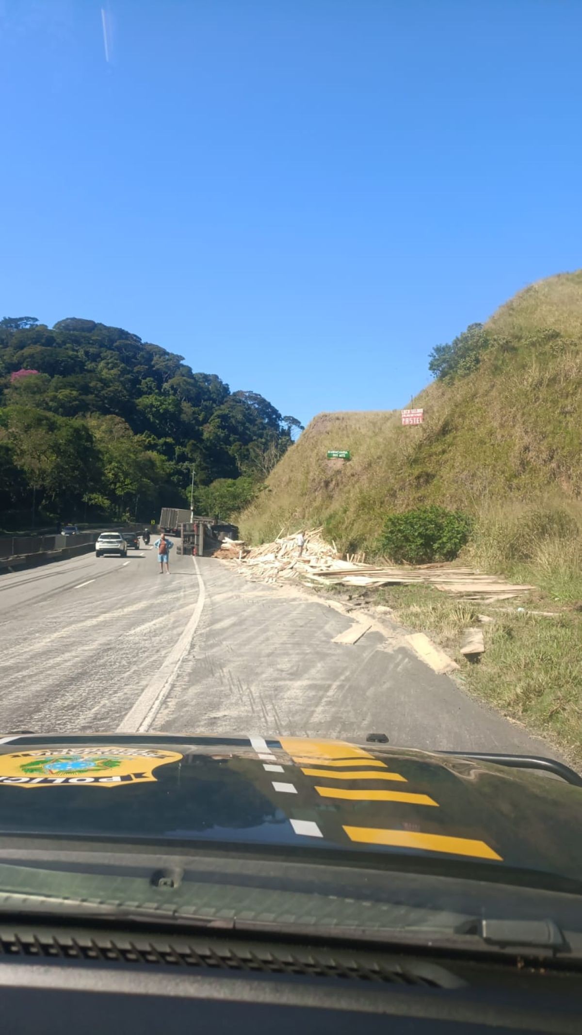 Carreta com carga de madeira tomba e deixa pessoa ferida na Via Dutra, em Piraí