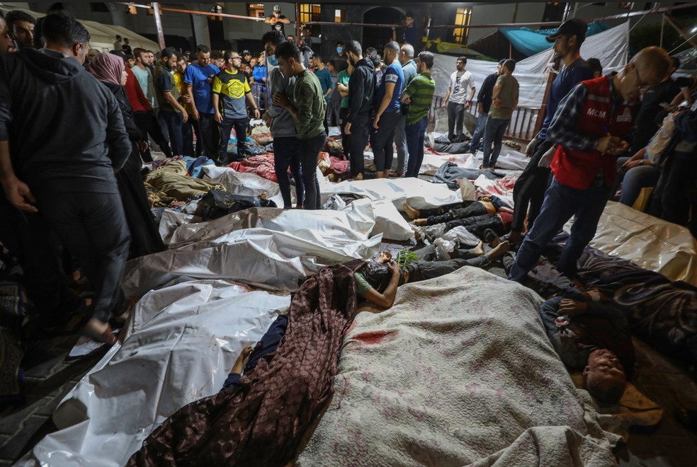 Pessoas ao redor de corpos de palestinos mortos em ataques de Israel ao hospital Ahli Arab, em Gaza; os corpos foram levados a outro hospital, o de Al-Shifa � Foto: Dawood Nemer/ AFP