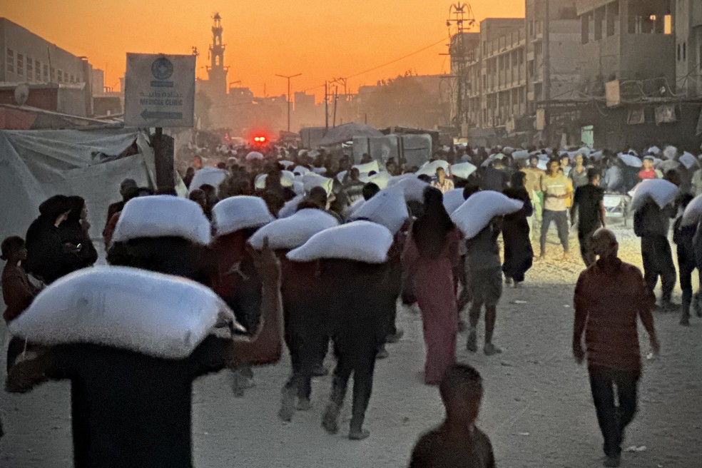 Homens caminham carregando sacos de farinha que foram retirados de um caminhão que transportava alimentos, em Khan Yunis, no sul da Faixa de Gaza, em 22 de julho de 2025 — Foto: AFP