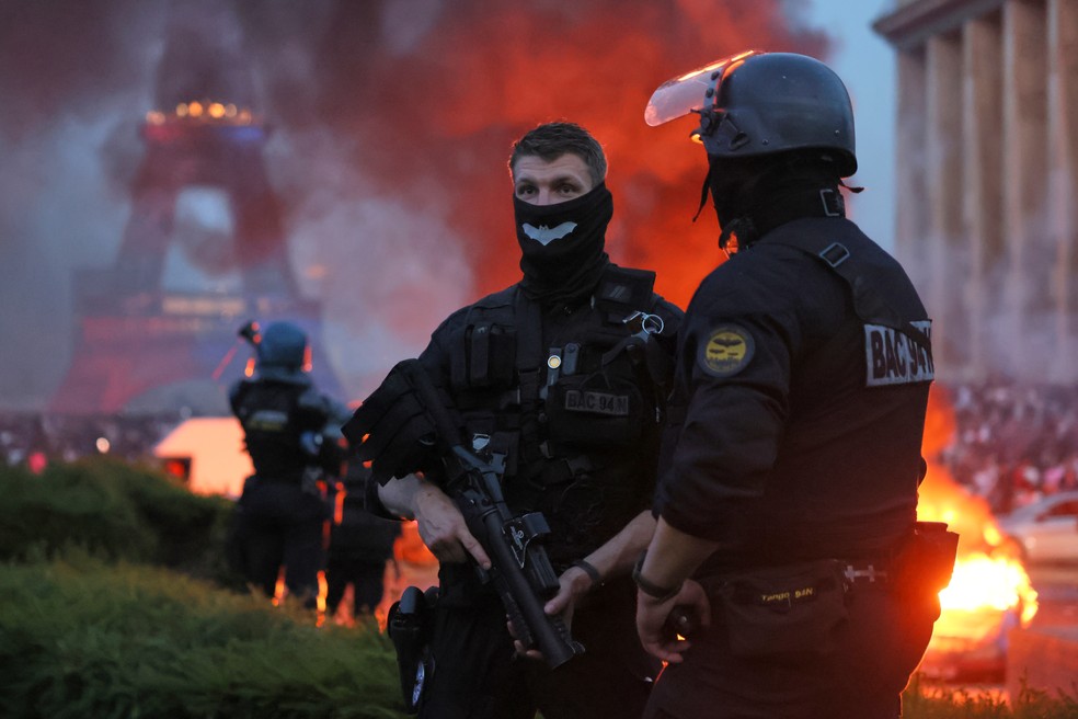 Carro pega fogo e fogos de artif&iacute;cio explodem enquanto a pol&iacute;cia observa torcedores do PSG comemorando em Paris, no s&aacute;bado, 30 de maio de 2026, ap&oacute;s a final da Liga dos Campe&otilde;es &mdash; Foto: Thomas Padilla/AP