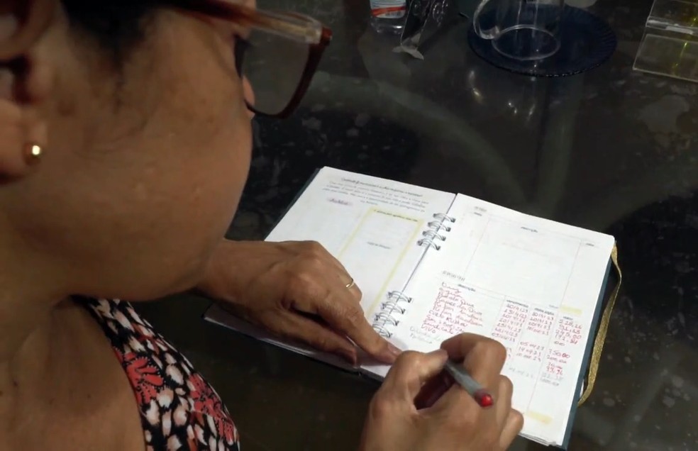 Mulher anotando dívidas em caderno de controle de gastos — Foto: Reprodução/TV Globo