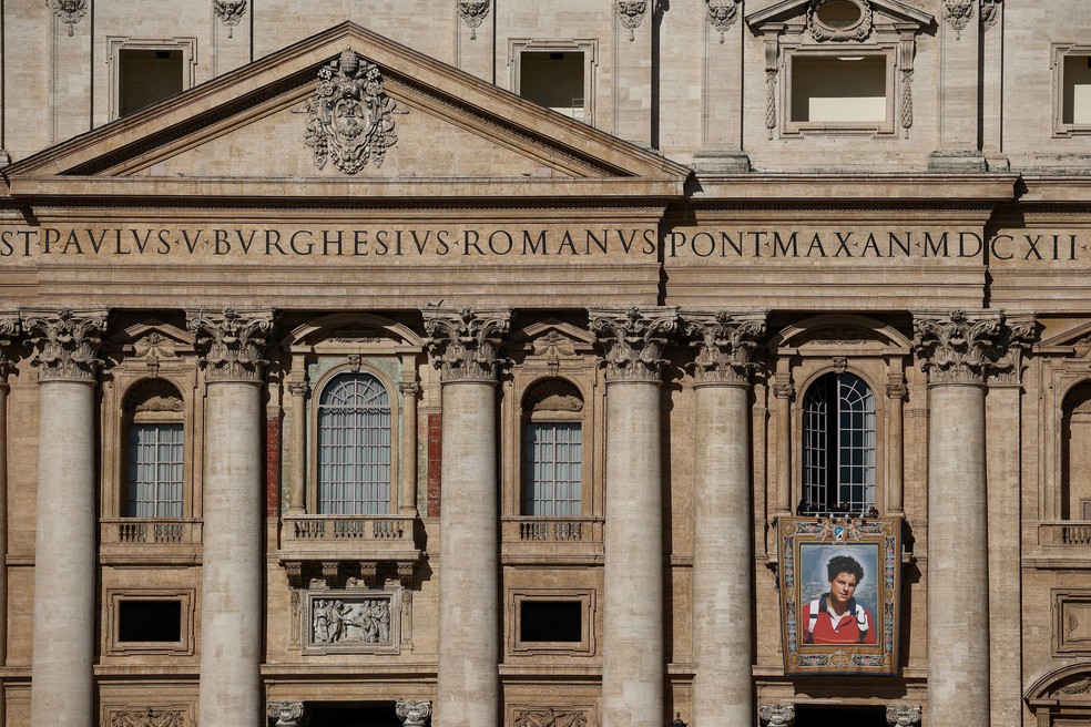 Imagem de Carlo Acutis, que se tornará 1º santo 'millenial' no domingo (7), é pendurada pelo Vaticano na Basílica de São Pedro em 4 de setembro de 2025. — Foto: REUTERS/Guglielmo Mangiapane