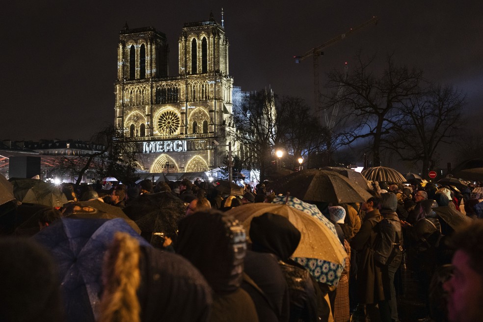 Público acompanhou cerimônia do lado de fora. Facha da catedral foi iluminada em noite fria em Paris — Foto: Bernat Armangue/AP Photo