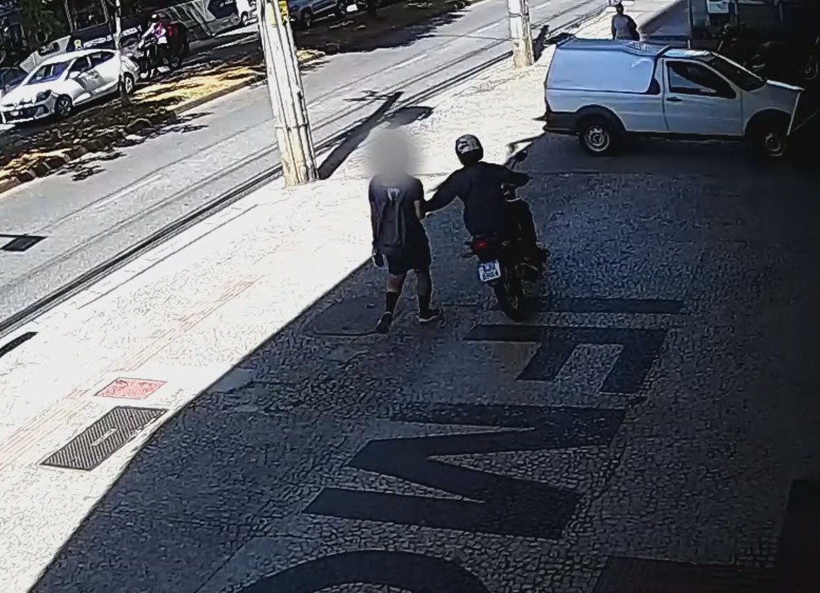 Motociclista invade calçada, arranca celular da mão de pedestre e foge; VÍDEO