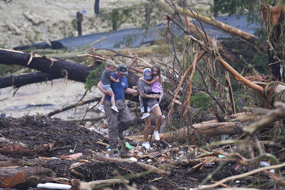 Família caminha sobre árvore caída após enchente que deixou mortos no Texas, em 5 de julho de 2025. — Foto: Julio Cortez/ AP