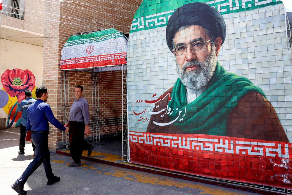Pessoas caminham pelas ruas de Teerã e passam por banner com imagem do aiatolá Mojtaba Khamenei. — Foto: AFP