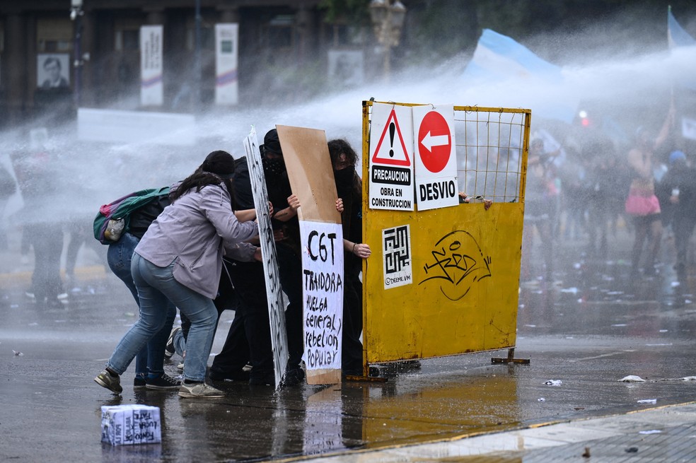 Manifestantes se protegem com escudos improvisados ​​contra jatos de água durante um protesto em apoio à comunidade universitária argentina, em 15 de outubro de 2026 — Foto: Pedro Lazaro Fernandez