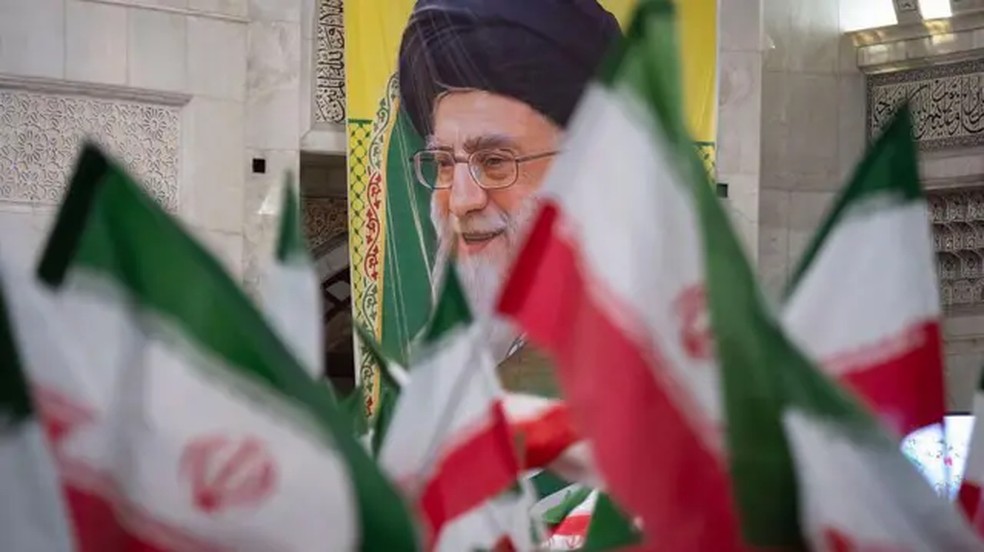 Bandeiras iranianas com um cartaz retratando o líder do país, Ali Khamenei, ao fundo. — Foto: Getty Images via BBC