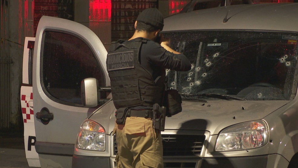 Agente da Polícia Civil faz perícia em veículo baleado — Foto: Reprodução/TV Globo