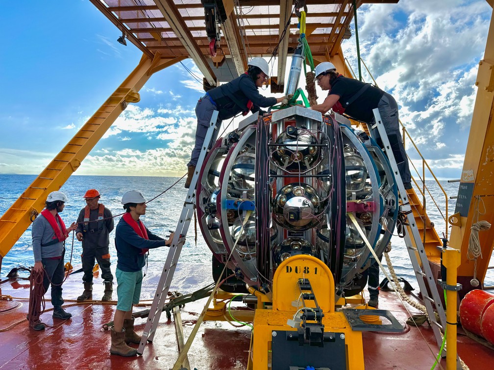 Pesquisadores fazem a inspeção final e conectam uma parte do telescópio subaquático ao guincho para a instalação. — Foto: Paschal Coyle/CNRS